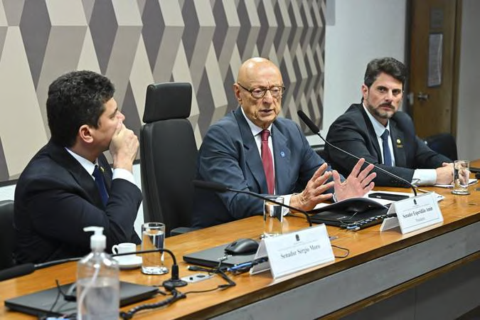 Three participants at the table, one speaking into a microphone.